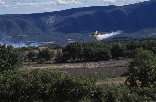 FRANCE, Provence Cote d’Azur, Luberon , Firefighter Plane flying towards smoke from a forest fire rising above green landscape.