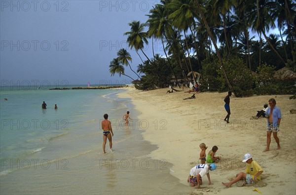 WEST INDIES, Tobago, Pigeon Point, People and children playing on shore of sandy beach fringed by palm trees.
