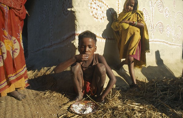 INDIA, Bihar, Myapur, "Boy in Ganges Plain village eating rice with his hands, little girl leaning against wall of building behind."