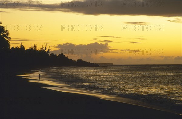 WEST INDIES, Tobago, Turtle Beach, Woman walking along the beach by the waters edge with yellow sunset at sea