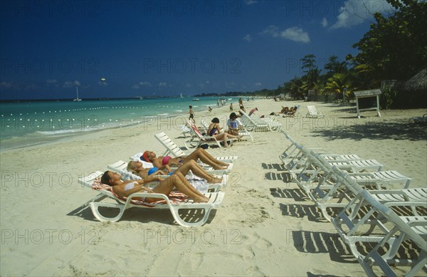 WEST INDIES,  Jamaica, Negril, Female tourists beach sunbathing on sun loungers facing away from the water