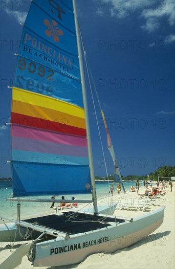 WEST INDIES, Jamaica, Negril, Catamaran with sail up on beach with tourists sunbathing and walking by water