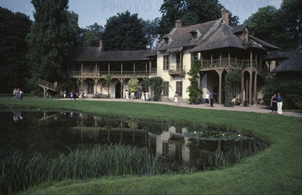 FRANCE, Ile de France, Paris, "Versailles.  The Queens Cottage in the Hamlet, exterior with tourist visitors reflected in pond."
