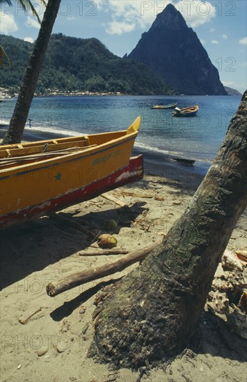 WEST INDIES, St Lucia, Soufriere, Fishing boat by coconut palm tree on beach with the Pitons in the distance
