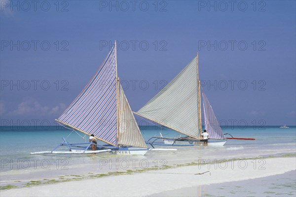 PHILIPPINES, Visayan Islands, Boracay Island, Two outriggers with striped sails moored on the edge of a sandy beach