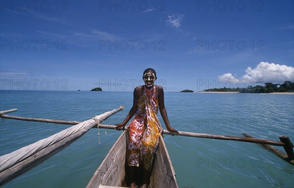 MADAGASCAR, Nosy Be, Young girl on a pirogue canoe wearing a colourful sarong and with her face painted.  Turquoise sea.