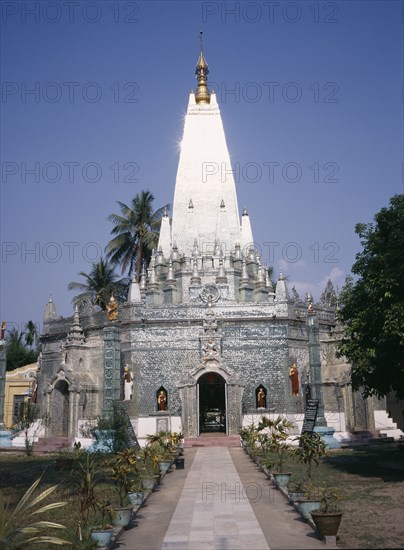 MYANMAR, Yangon, "Buddhist temple exterior with the sun reflecting off the silver spire, view along path towards the entrance. "