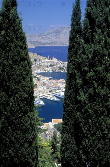 GREECE, Dodecanese, Symi, Gialo.  The town and harbour partly viewed between trees in the foreground.