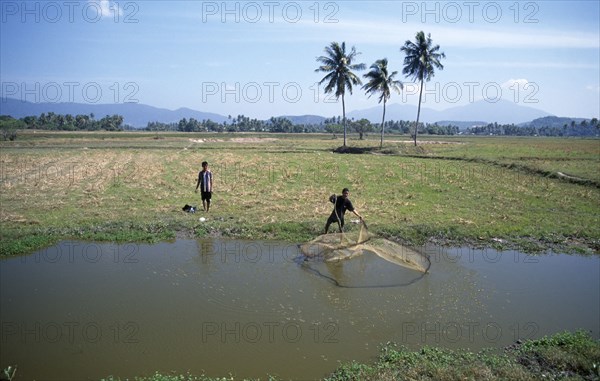 MALAYSIA, Kedah, Langkawi, Two men by pond in fields near Cenang with one casting a fishing net into the water