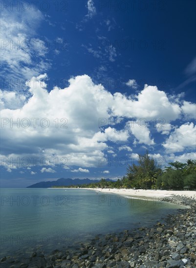 MALAYSIA, Langkawi, Kedah, Pantai Cenang beach looking towards Gunung Mat Cincang with a stoney beach in the foreground