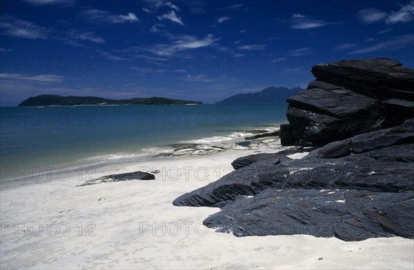 MALAYSIA, Kedah, Langkawi, Pantai Tengah beach looking towards Pulau Rebak Besar island with rocks in the foreground