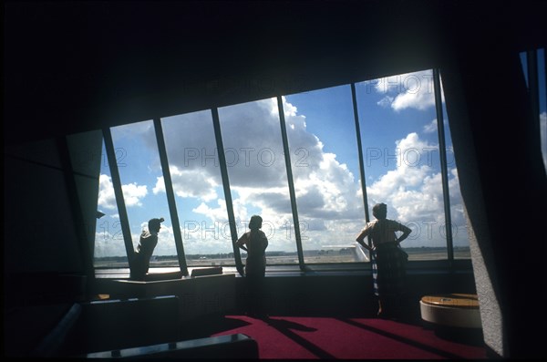 USA, Florida, Miami, Miami Airport. Three figures looking out of window towards planes framed by interior walls in heavy shadow.