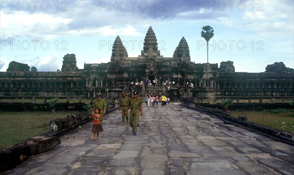 CAMBODIA, Siem Reap, Angkor Wat, "View along wide stone path towards temples and visitors, small girl and temple guards in the foreground."