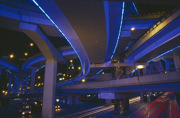 CHINA, Shanghai, "Bridge and intersecting roads seen from below, lit by ultra violet light at night with traffic light trails."