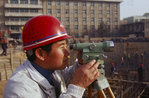 CHINA, Shaanxi Province, Xian, Surveyor using a theodolite working on a building construction site.