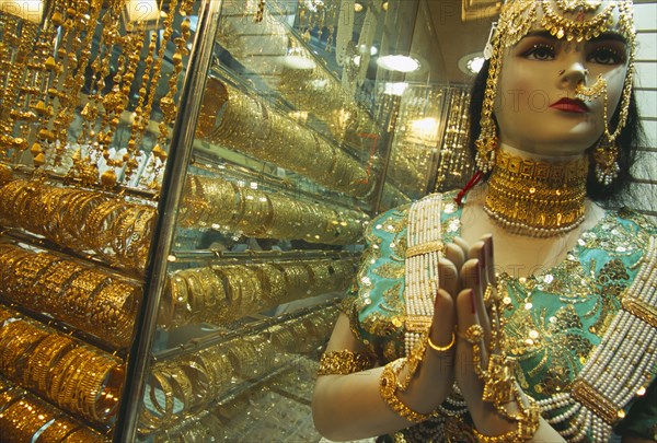 UAE, Dubai, The Gold Souk.  Shop window display with mannequin draped in gold jewellery beside large display of gold bracelets.