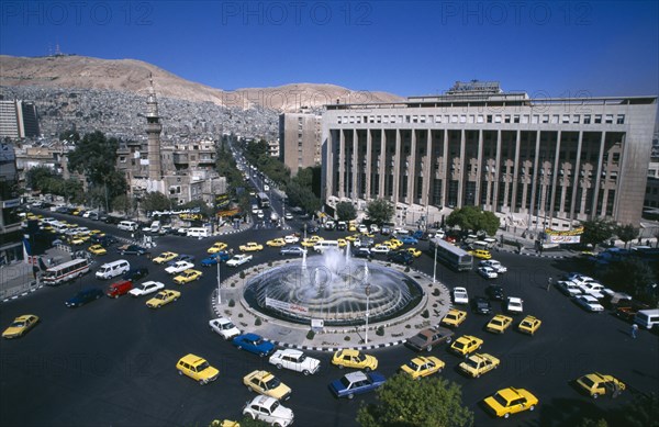 SYRIA, South, Damascus, View over Tajrida Al Maghribiya Square with traffic encircling a central fountain.  Modern facade of the Central Bank top right.