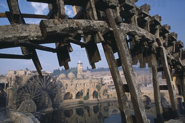 SYRIA, Central, Hama, Wooden norias or waterwheels on the Orontes river.  Part view of wheel section in the foreground framing the Al-Nuri Mosque dating from 1172 and built of limestone and basalt.