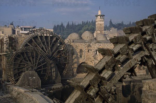 SYRIA, Central, Hama, Wooden norias or waterwheels on the Orontes river and the Al-Nuri Mosque dating from 1172 and built of limestone and basalt. Section of wheel in the immediate foreground.