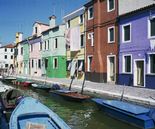 ITALY, Veneto, Venice, Burano Island.  Tenders moored in canal outside row of brightly painted fisherman’s houses.