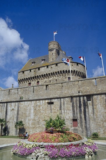 FRANCE, Brittany, Ille et Vilaine, "St. Malo.  Chateau Gaillard, exterior with flags flying from crenellated wall and water feature with central flowerbed in the foreground."