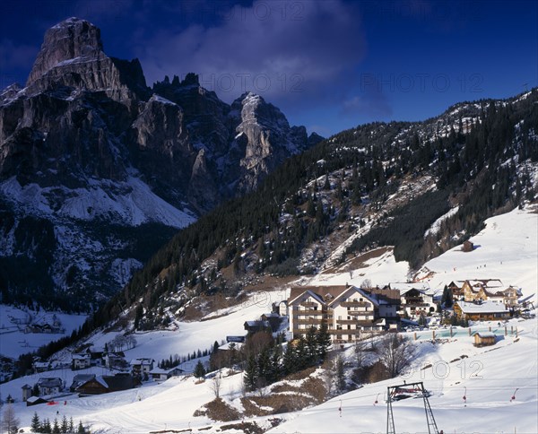 ITALY, Trentino-Alto Adige, Dolomites, Corvara.  Hotels and other buildings in snow covered valley with mountains behind.