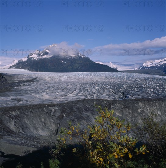 USA, Alaska, Sheritan Glacier, Glacier near Cordova with the Alaska mountain range in the background.  Tree branches with green and yellow leaves in the foreground.