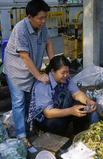 THAILAND, North, Chiang Mai, Wholesale Food Market.  Female vendor seated at vegetable stall having her shoulders massaged.