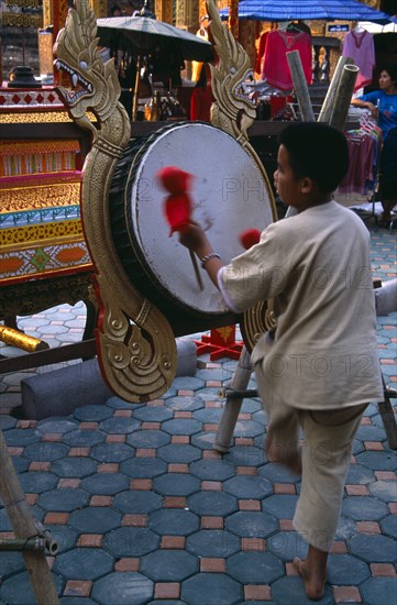 THAILAND, North, Chiang Mai, Wat Chettawan on Tha Phae Road.  Young boy playing drum suspended on frame with red and gold dragon carvings.