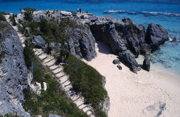 BERMUDA, Warwick, Astwood Park, Two people standing on cliff top above empty sandy beach with steps leading down to it at the side.