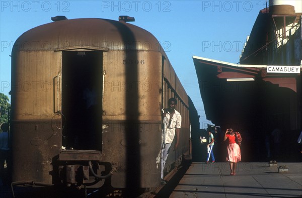 CUBA, Camaguey, Railway carriages alongside the platform of Camaguey station with a man holding onto a carriage door with a woman walking past