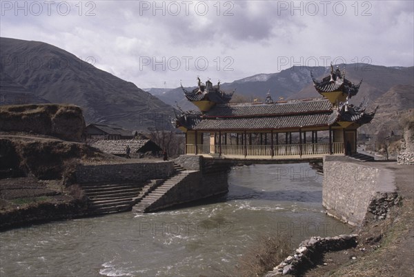 CHINA, Sichuan Province, Songpan, Chinese bridge with pagoda style roof over river in mountain landscape