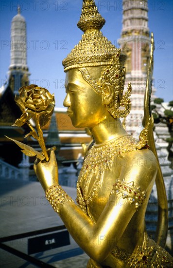 THAILAND, Bangkok, Wat Phra Kaew, Or Royal Palace. Golden temple statue of a figure holding a flower