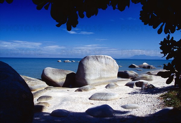 MALAYSIA, Penang, Batu Ferringhi, "Beach and large, smooth rocks part framed by silhouetted tree branches."