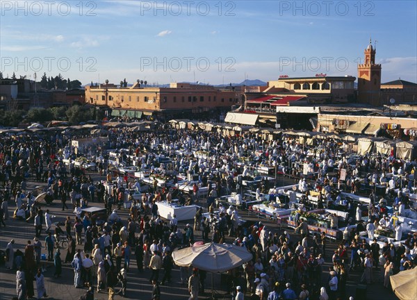 MOROCCO, Marrakech, "Djemma El Fina. Elevated view over busy market square, crowds of people around stalls with buildings behind."