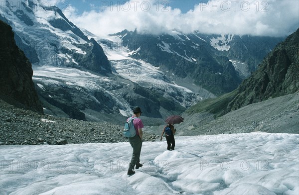 RUSSIA, Caucasus Mountains, Adyr Su Valley, Hikers walking down glacier wearing sun glasses and carrying umbrella to protect against sun.