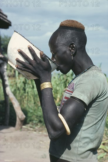 SUDAN, Tribal Peoples, Dinka man drinking groundnut gruel at ceremony welcoming young men back to village after spending eight weeks at fattening camp.