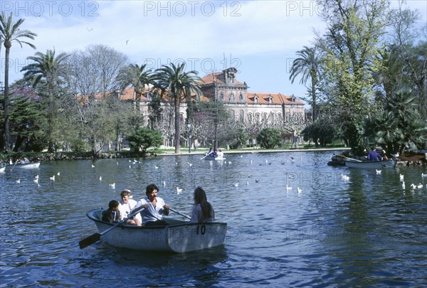 SPAIN, Catalonia, Barcelona, Family in rowing boat on lake in front of the Catalan Parliament building in Parc de la Cuitadella