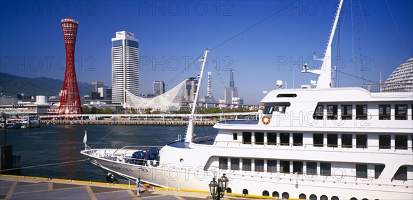 JAPAN, Honshu, Kobe, View over the port area with moored passenger ferry in the foreground and the Port Tower and city skyline behind