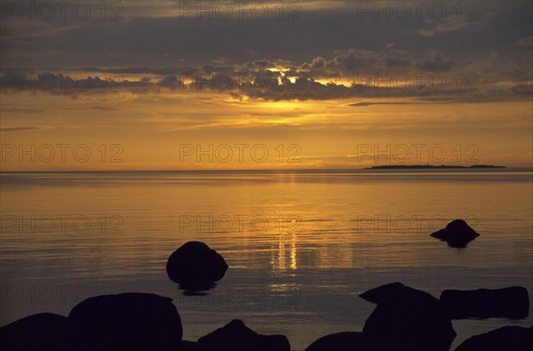 ESTONIA, Sunset, Sunset over water with rocks in the foreground on the ...