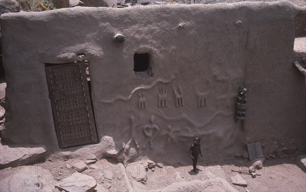 MALI, Dogon village, Detail of exterior wall and door of chiefs house with small child standing outside.
