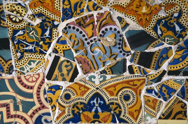 SPAIN, Catalonia, Barcelona, Parc Guell.  Detail of colourful mosaic by Gaudi from a park bench seat.