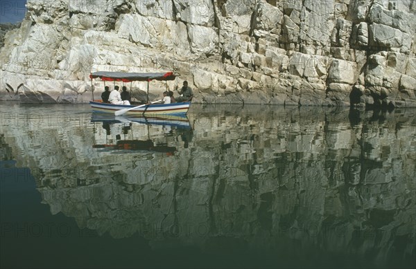 INDIA, Madhya Pradesh, Marble Rocks, Painted tourist boat on the Narmada River passing sheer cliffs reflected in water.