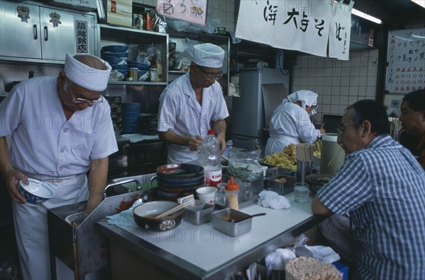 JAPAN, Honshu, Tokyo, Tsukiji Fish Market. Chefs working in the open kitchen of a food bar with customers sitting at the counter