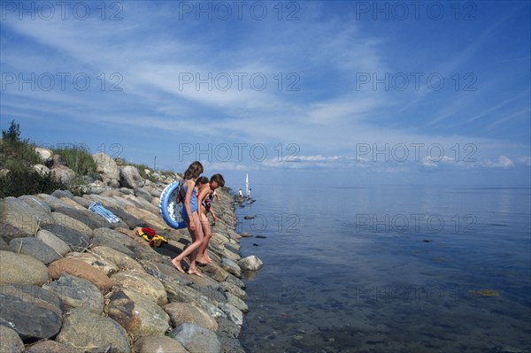 ESTONIA, Kihnu Island, Group of young girls wlking down stone sea defence into water off the Baltic coast.