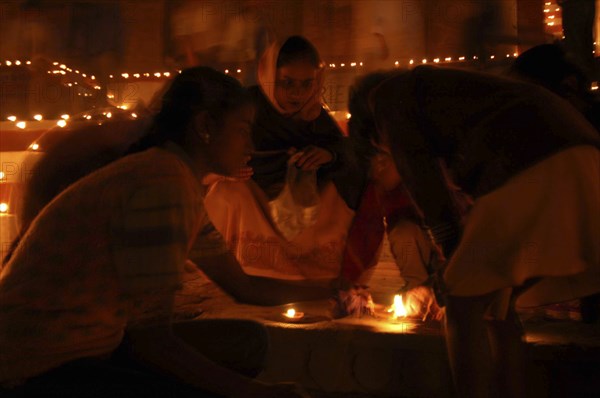 INDIA, Uttar Pradesh, Varanasi, Deep Diwali Festival with young girls lighting oil lamps on steps leading down to the Ganges River