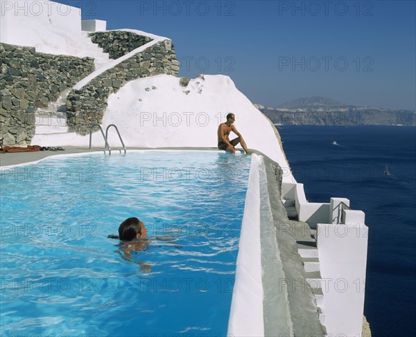 GREECE, Cyclades Islands, Santorini, Imerovigli.  Couple in swimming pool overlooking sea.