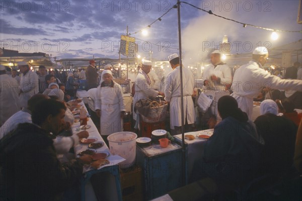 MOROCCO, Marrakesh, Djemaa el Fna. Food vendors serving up food to hungry customers seated around them at dusk