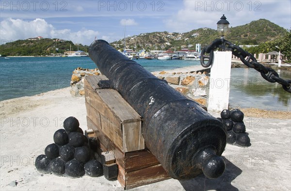 WEST INDIES, St Vincent & The Grenadines, Union Island, Ancient canon on the harbourside at Clifton with the town and moorings in the distance