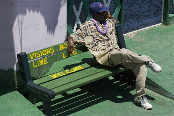 WEST INDIES, St Vincent & The Grenadines, Union Island, Man sitting on pavement bench in Clifton